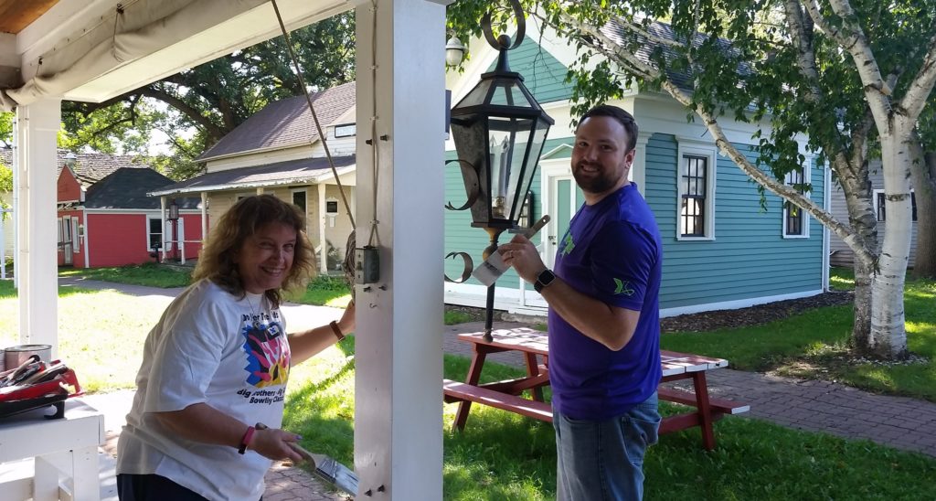 woman and man volunteer painting a column with white paint on a fond du lac building